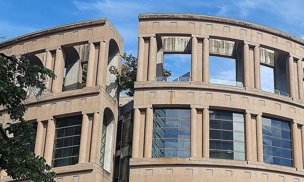 Close-up of the top two floors of Vancouver Public Library Central Branch, framed by trees against a clear blue sky.
