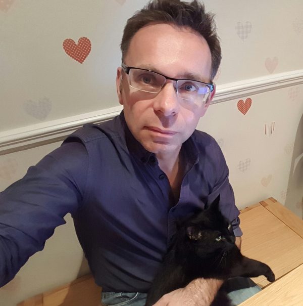 A seated man taking a selfie with a black cat
